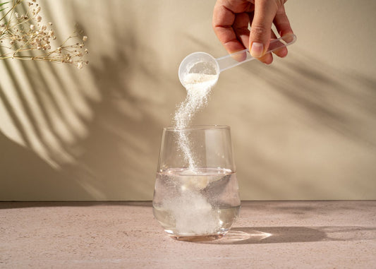 Vue sur la main d’une personne versant de la poudre de collagène blanche dans un verre transparent à l’aide d’un doseur