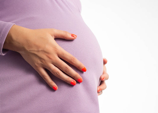 Femme enceinte aux ongles vernis rouge tenant son ventre rond, haut lilas, fond blanc