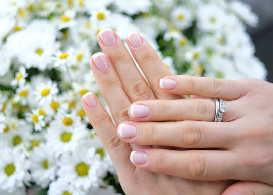 Au premier plan, des mains arborant une french manucure discrète, un bouquet de marguerites au second plan